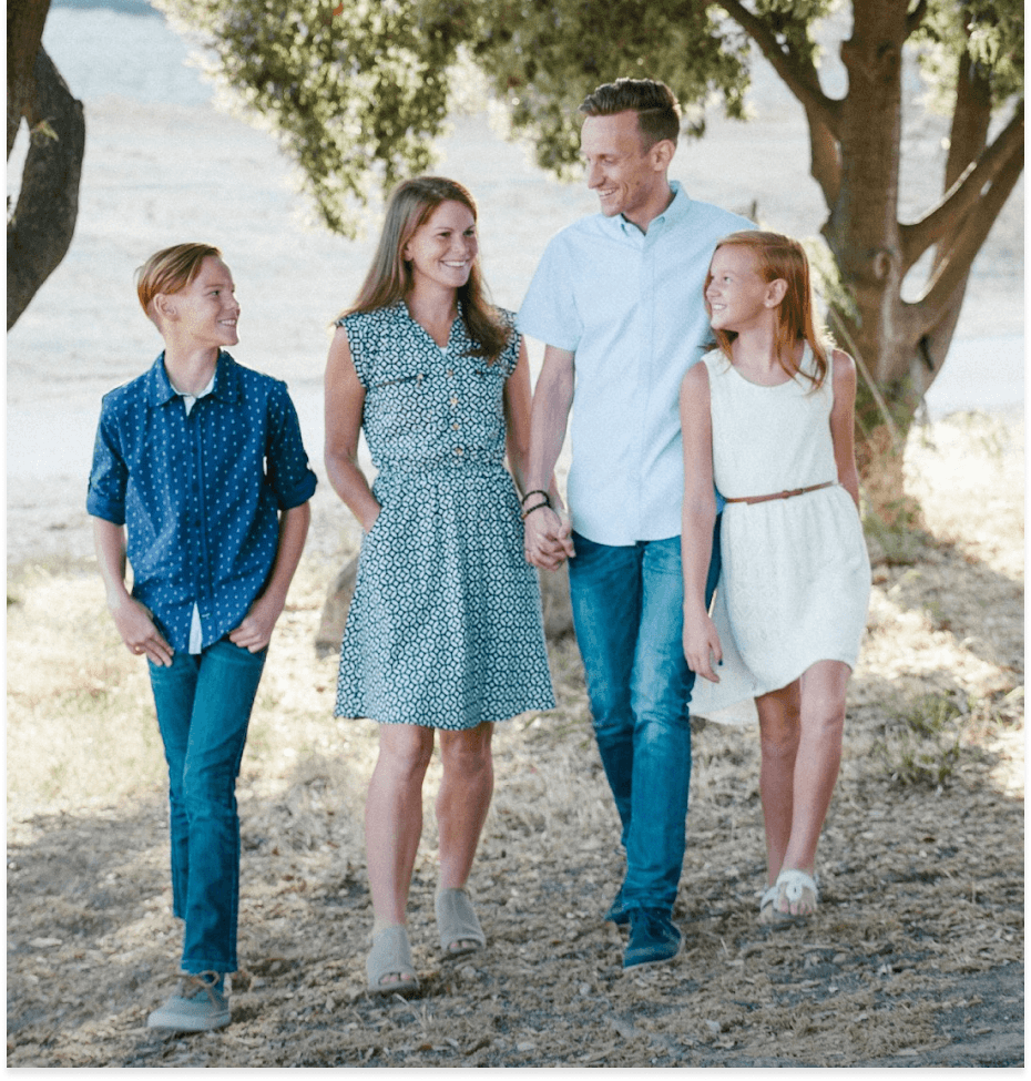 A happy family of four – a man, woman, boy, and girl – smiling and walking together outdoors.