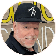 Smiling man with a white beard and blue eyes wearing a black baseball cap with a white "AR" logo.